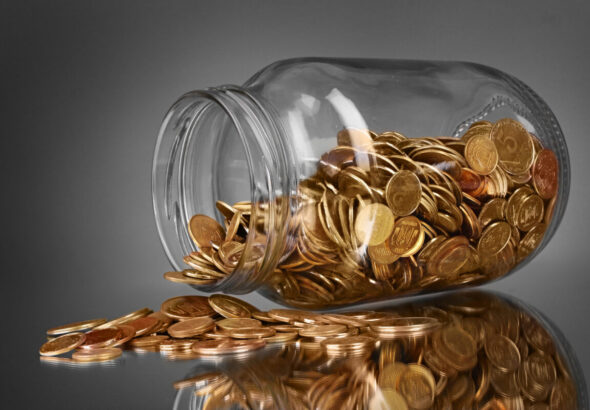 coins spilling from a money jar on gray background